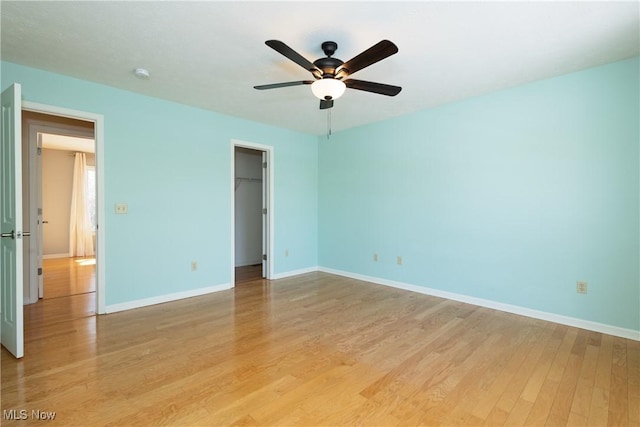 unfurnished bedroom featuring ceiling fan, a spacious closet, light hardwood / wood-style floors, and a closet