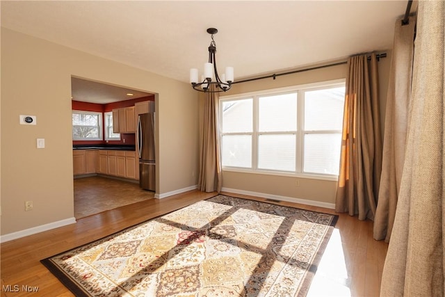 unfurnished dining area with an inviting chandelier and light wood-type flooring