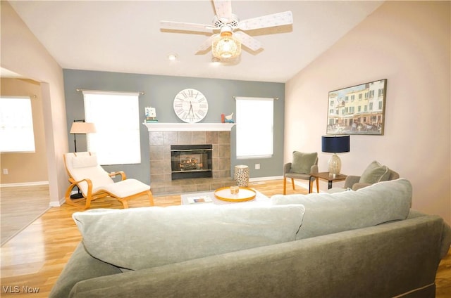 living room with a tiled fireplace, ceiling fan, wood-type flooring, and vaulted ceiling