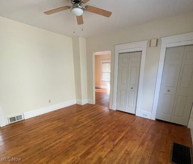 unfurnished bedroom featuring hardwood / wood-style flooring, ceiling fan, and multiple closets