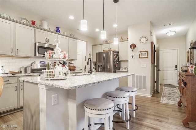 kitchen with appliances with stainless steel finishes, backsplash, a center island with sink, and hanging light fixtures