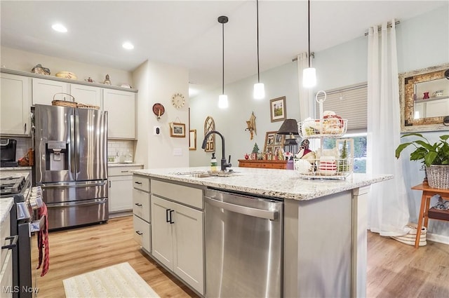 kitchen featuring sink, decorative backsplash, an island with sink, appliances with stainless steel finishes, and decorative light fixtures