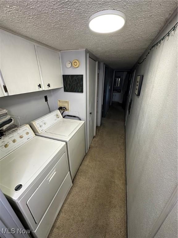 laundry room with washer and dryer, cabinets, light colored carpet, and a textured ceiling