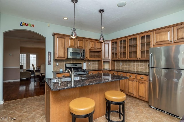 kitchen featuring sink, a kitchen island with sink, stainless steel appliances, decorative backsplash, and decorative light fixtures