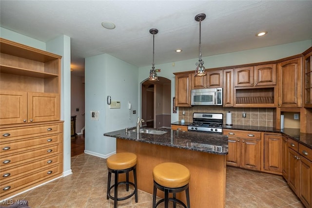 kitchen featuring sink, appliances with stainless steel finishes, hanging light fixtures, a center island with sink, and decorative backsplash