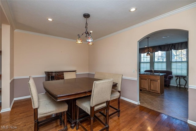 dining area featuring ornamental molding, dark wood-type flooring, a notable chandelier, and a textured ceiling