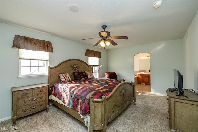 bedroom featuring multiple windows, connected bathroom, light carpet, and ceiling fan