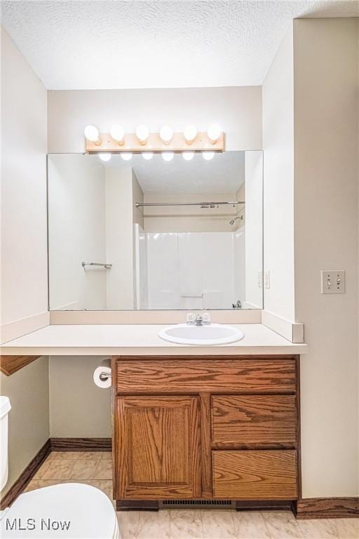 bathroom featuring a textured ceiling, toilet, walk in shower, and vanity