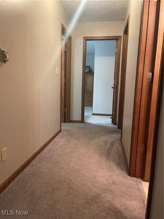 hallway featuring light colored carpet and a textured ceiling