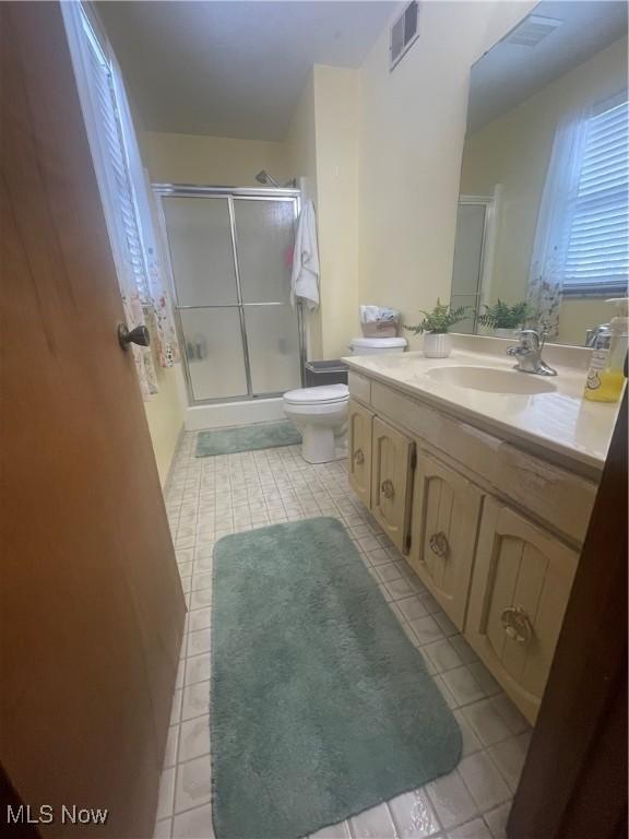 bathroom with tile patterned floors, vanity, toilet, and a shower with shower door