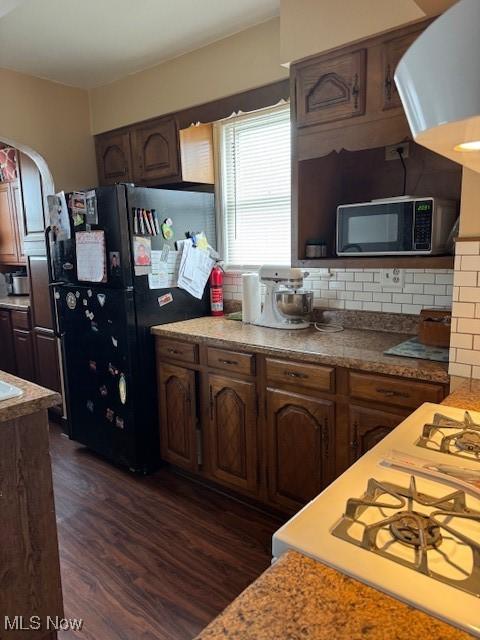 kitchen with backsplash, dark brown cabinetry, dark hardwood / wood-style flooring, and black appliances