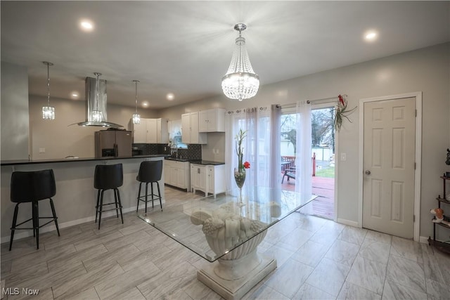 kitchen featuring island exhaust hood, tasteful backsplash, decorative light fixtures, stainless steel fridge with ice dispenser, and white cabinetry