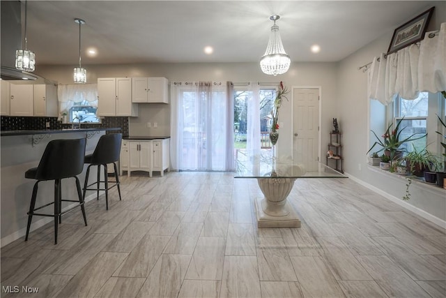 kitchen with sink, an inviting chandelier, tasteful backsplash, pendant lighting, and white cabinets