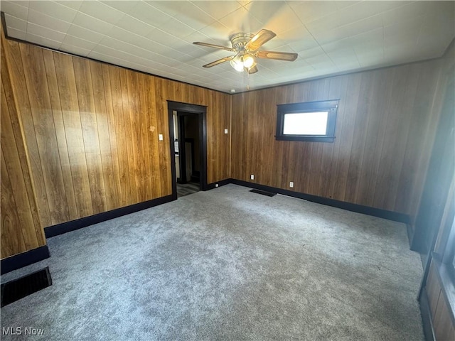 carpeted spare room featuring ceiling fan and wooden walls