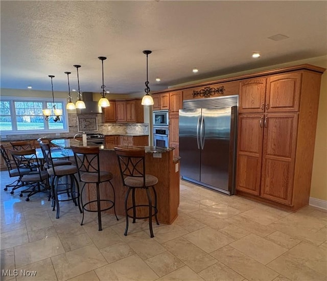 kitchen featuring a large island, built in appliances, pendant lighting, extractor fan, and a breakfast bar area