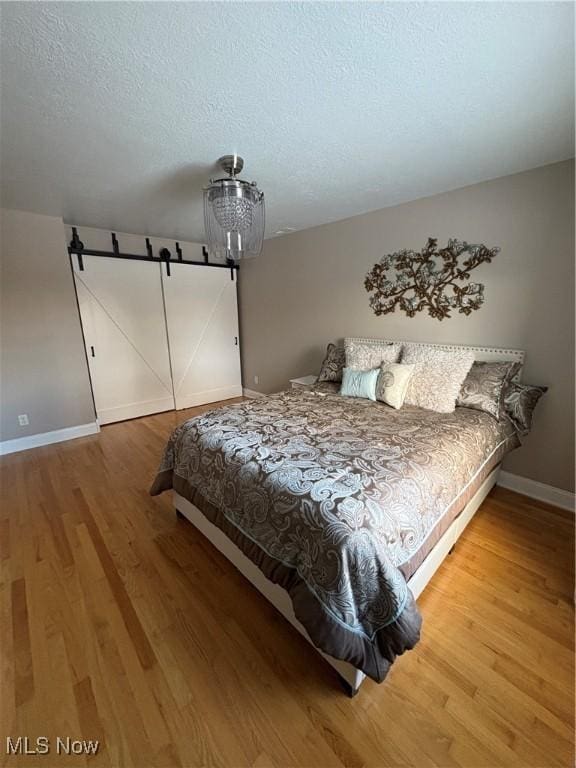 bedroom featuring wood-type flooring, a barn door, and a textured ceiling