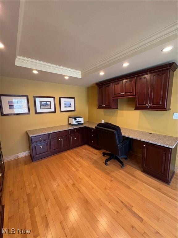 office area featuring built in desk, light hardwood / wood-style flooring, a raised ceiling, and ornamental molding