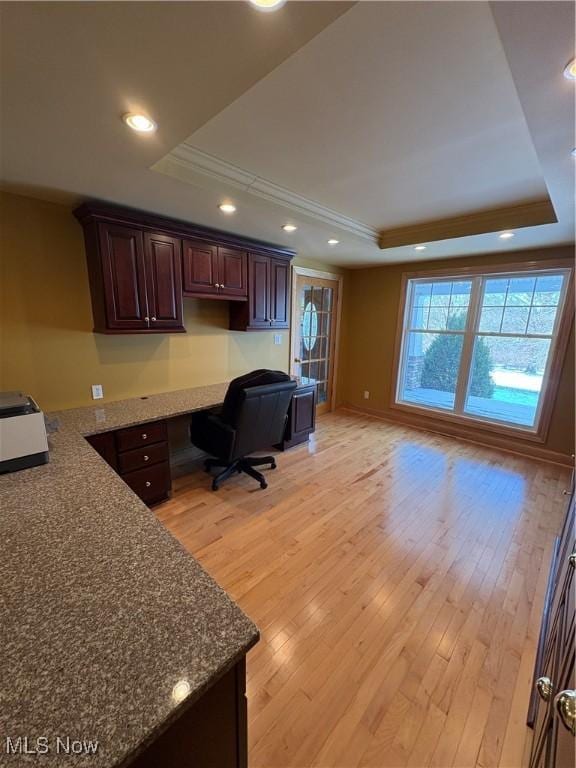 home office with light hardwood / wood-style floors, built in desk, ornamental molding, and a tray ceiling