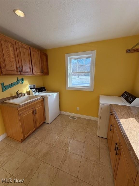 laundry room with cabinets, a textured ceiling, sink, light tile patterned floors, and separate washer and dryer