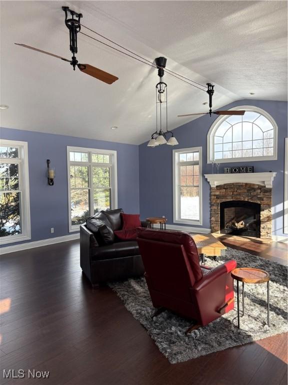 living room with hardwood / wood-style flooring, a stone fireplace, ceiling fan, and lofted ceiling