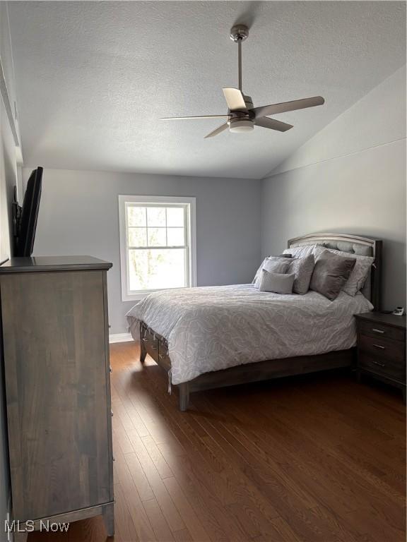 bedroom with a textured ceiling, dark hardwood / wood-style flooring, vaulted ceiling, and ceiling fan