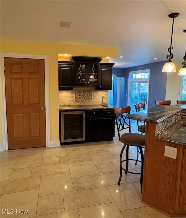 kitchen featuring decorative backsplash, a kitchen breakfast bar, beverage cooler, sink, and pendant lighting