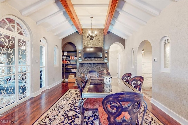 dining area featuring built in shelves, hardwood / wood-style flooring, a chandelier, vaulted ceiling with beams, and a stone fireplace