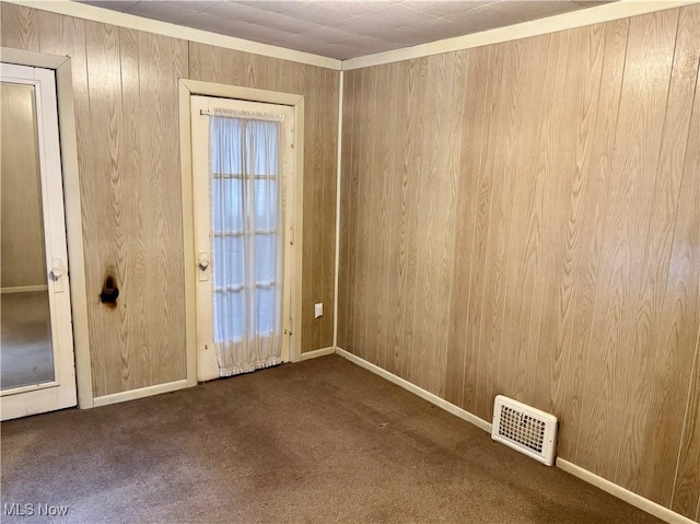 carpeted empty room featuring wood walls and crown molding