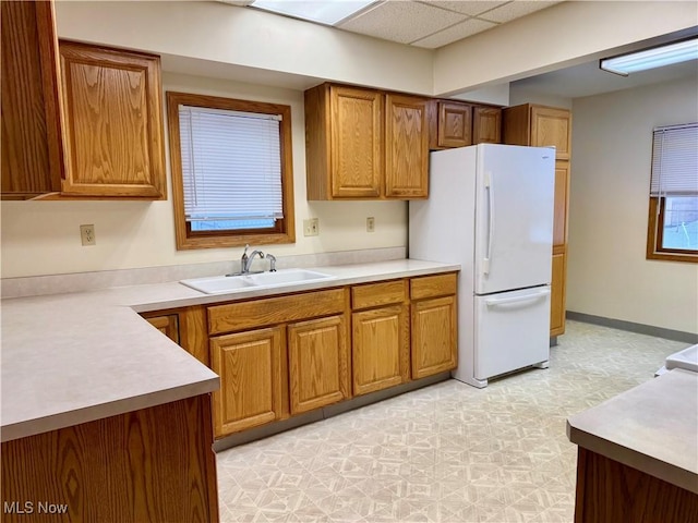 kitchen with white refrigerator, a drop ceiling, and sink