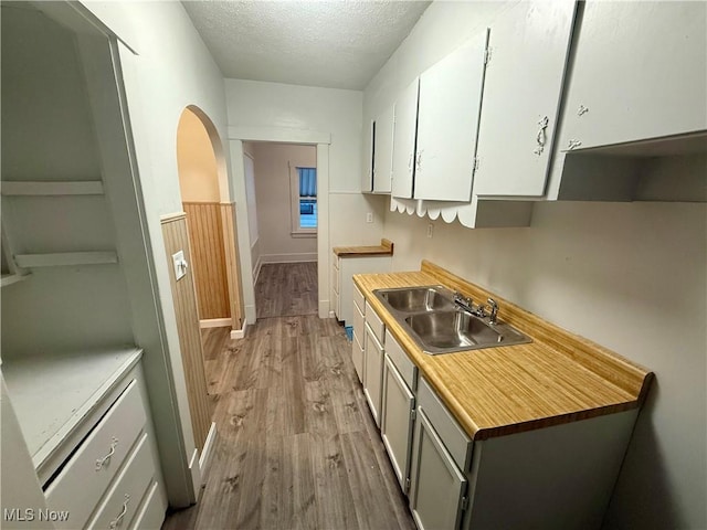 kitchen featuring a textured ceiling, light hardwood / wood-style floors, white cabinetry, and sink