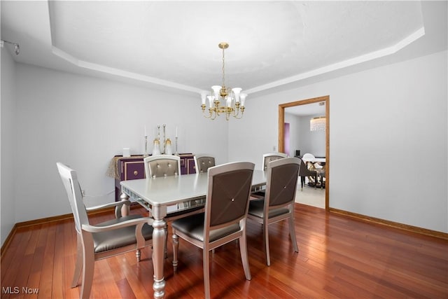 dining space featuring wood-type flooring, a raised ceiling, and an inviting chandelier