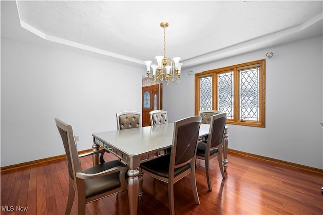 dining space with a raised ceiling, hardwood / wood-style floors, and a notable chandelier