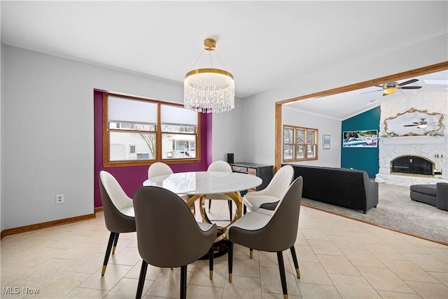 dining room featuring light carpet, a stone fireplace, vaulted ceiling, ornamental molding, and ceiling fan with notable chandelier