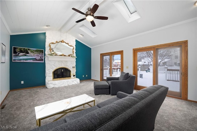 living room featuring a stone fireplace, ceiling fan, carpet, vaulted ceiling with skylight, and ornamental molding