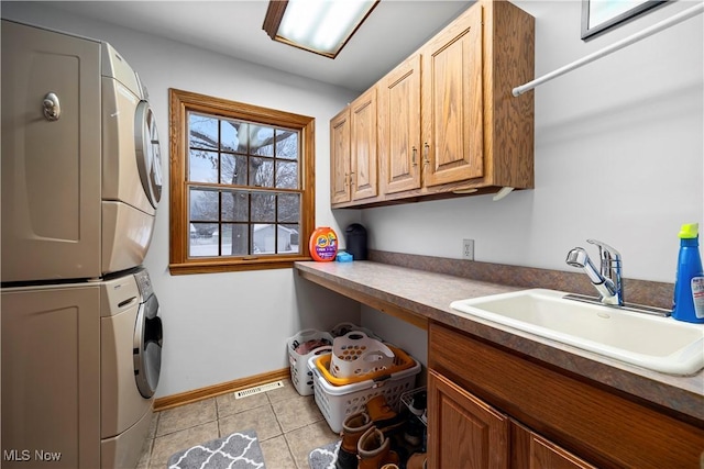 laundry room with stacked washer and clothes dryer, a sink, cabinet space, light tile patterned flooring, and baseboards