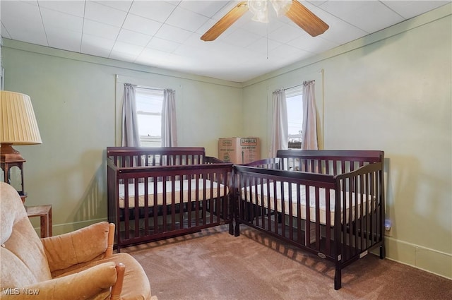 bedroom featuring a crib, multiple windows, carpet floors, and ceiling fan