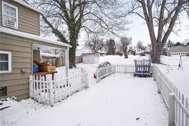 snowy yard featuring a storage unit and a trampoline