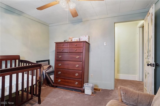 carpeted bedroom featuring ceiling fan and a crib