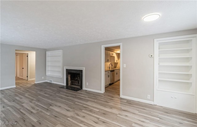 unfurnished living room featuring built in features, light wood-type flooring, a textured ceiling, and sink