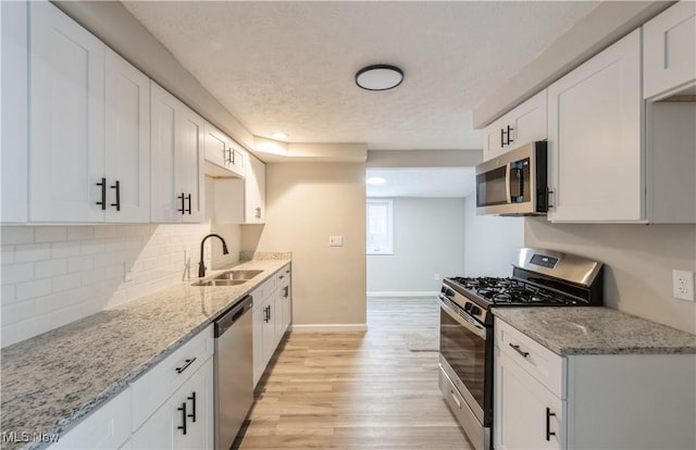 kitchen with sink, light stone counters, appliances with stainless steel finishes, white cabinets, and light wood-type flooring