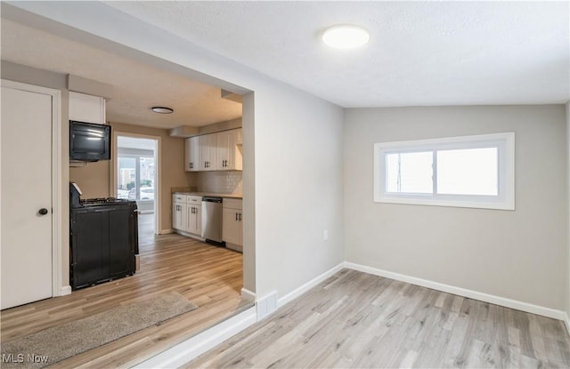 kitchen featuring decorative backsplash, white cabinetry, black appliances, and light wood-type flooring