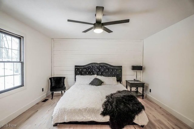 bedroom featuring ceiling fan, wooden walls, and light hardwood / wood-style floors