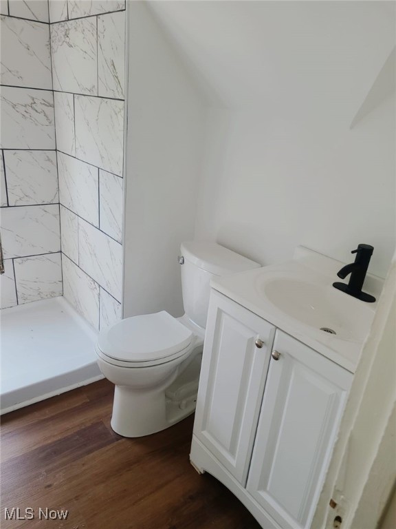 bathroom with tiled shower, hardwood / wood-style floors, vanity, and toilet