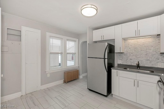 kitchen featuring radiator, sink, backsplash, white cabinets, and appliances with stainless steel finishes