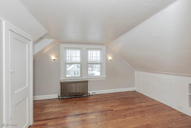 additional living space featuring radiator heating unit, wood-type flooring, and vaulted ceiling