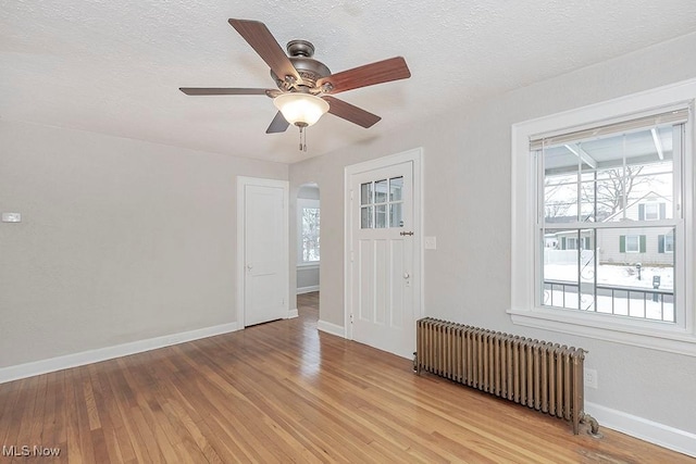 unfurnished room featuring radiator, ceiling fan, a textured ceiling, and light wood-type flooring