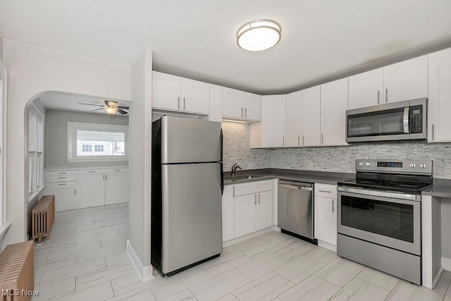 kitchen featuring appliances with stainless steel finishes, backsplash, radiator, sink, and white cabinets