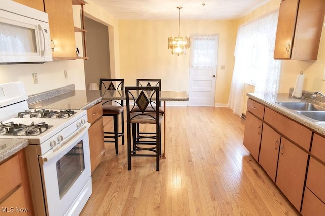 kitchen with light wood-type flooring, a breakfast bar, white appliances, sink, and hanging light fixtures