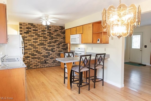 kitchen featuring white appliances, ceiling fan with notable chandelier, sink, light hardwood / wood-style floors, and brick wall