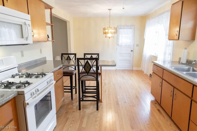 kitchen featuring a kitchen bar, white appliances, sink, decorative light fixtures, and light hardwood / wood-style floors